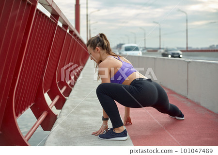 Girl athlete stretching in the morning outside, in the city, on modern bridge crossing river. Active healthy lifestyle. Sport and recreation concept. Girl athlete stretching in the morning outside, in the city, on modern bridge crossing river. Active healthy lifestyle. Sport and recreation concept. 101047489