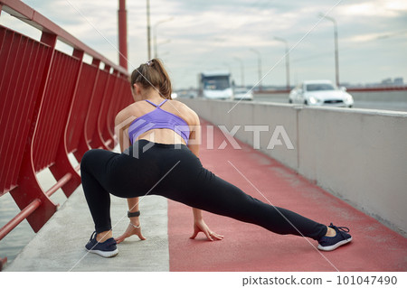 Girl athlete stretching in the morning outside, in the city, on modern bridge crossing river. Active healthy lifestyle. Sport and recreation concept. Girl athlete stretching in the morning outside, in the city, on modern bridge crossing river. Active healthy lifestyle. Sport and recreation concept. 101047490