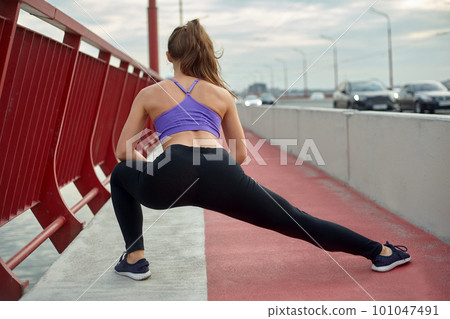 Girl athlete stretching in the morning outside, in the city, on modern bridge crossing river. Active healthy lifestyle. Sport and recreation concept. Girl athlete stretching in the morning outside, in the city, on modern bridge crossing river. Active healthy lifestyle. Sport and recreation concept. 101047491