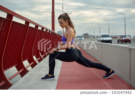 Girl athlete stretching in the morning outside, in the city, on modern bridge crossing river. Active healthy lifestyle. Sport and recreation concept. Girl athlete stretching in the morning outside, in the city, on modern bridge crossing river. Active healthy lifestyle. Sport and recreation concept. 101047492