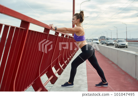 Girl athlete stretching in the morning outside, in the city, on modern bridge crossing river. Active healthy lifestyle. Sport and recreation concept. Girl athlete stretching in the morning outside, in the city, on modern bridge crossing river. Active healthy lifestyle. Sport and recreation concept. 101047495