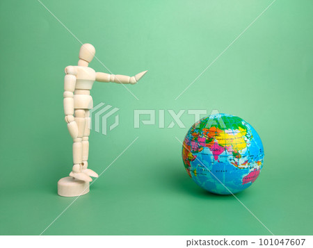 Wooden mannequin and earth globe on a green background Wooden mannequin and earth globe on a green background 101047607