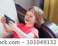 Close-up smiling girl lies in an armchair in a room by the window and using phone 101049132