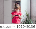 Smiling girl stands in a room by the window and using phone 101049136