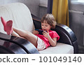 Smiling girl lies in an armchair in a room by the window and and using phone 101049140