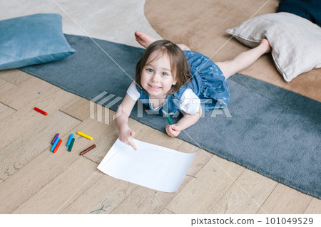 A two-year-old girl lies on the floor and draws with pencils. 101049529