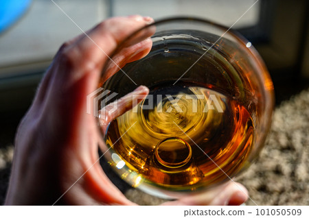 Caucasian hand holding a glass of amber colored liquid with a wedding ring at the bottom 101050509