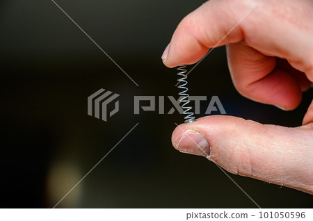 Caucasian hand compressing a metal spring between a thumb and finger 101050596