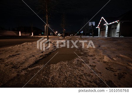 Ice and snow on a sidewalk at night with streetlight reflecting off the slick surface. 101050768