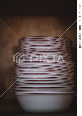 Narrow depth of field picture of an open kitchen cabinet stacked ceramic plates and bowls. 101050852