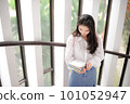 Young woman standing near the glass door and looking down at some notebooks 101052947