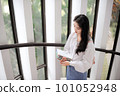 Young woman standing near the glass door and holding some notebooks 101052948