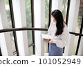 Young woman holding some notebooks near the glass door in the daytime 101052949