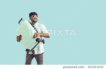 Happy excited indian guy tourist or vacationer holding travel suitcase on light blue background. Happy excited indian guy tourist or vacationer holding travel suitcase on light blue background. 101053245