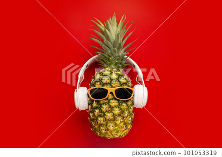 Ripe pineapple with sunglasses and headphones on red background Ripe pineapple with sunglasses and headphones on red background 101053319