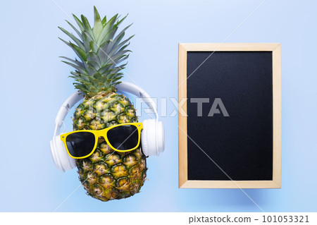 Pineapple in sunglasses and headphones with empty blackboard on blue background Pineapple in sunglasses and headphones with empty blackboard on blue background 101053321