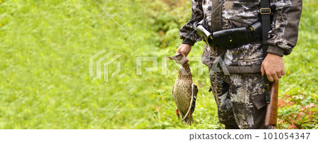 A man in a camouflage uniform with a gun holds a duck in his hands. A man in a camouflage uniform with a gun holds a duck in his hands. 101054347