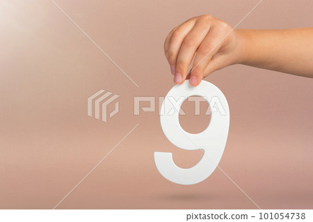 Number nine in hand. A hand holds a white number 9 on a red background. Concept with number nine. Birthday 9 years, percentage, ninth grade or day. 101054738
