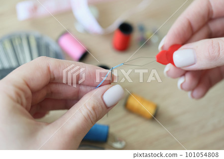 Hands of woman using special tool for threading blue needle Hands of woman using special tool for threading blue needle 101054808