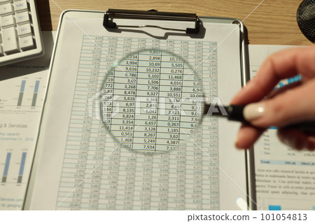Hand of woman holding magnifier glass over accounting papers Hand of woman holding magnifier glass over accounting papers 101054813
