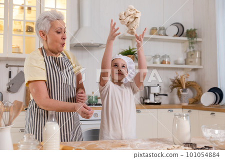 Happy family in kitchen. Grandmother and granddaughter child cook in kitchen together. Grandma teaching kid girl knead dough bake cookies. Household teamwork helping family generations concept 101054884