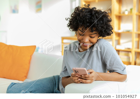 African girl holding smartphone touch screen typing scroll page at home. Woman with cell phone surfing internet using social media apps playing game. Shopping online Internet news cellphone addiction African girl holding smartphone touch screen typing scroll page at home. Woman with cell phone surfing internet using social media apps playing game. Shopping online Internet news cellphone addiction 101054927