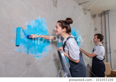 Couple in new home during repair works painting wall together. Happy family holding paint roller painting wall with blue color paint in new house. Home renovation DIY renew home concept Couple in new home during repair works painting wall together. Happy family holding paint roller painting wall with blue color paint in new house. Home renovation DIY renew home concept 101055109