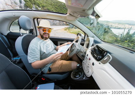 Hipster man looking on location navigation map in car, tourist traveler driving and hold in male hands europe cartography, view and plan tourist way road, trip in transportation cabriolet auto 101055270