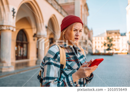 Upset sad angry traveler woman in style clothes has received bad sms, text message in old city street of Krakow, Poland. Negative emotion 101055649