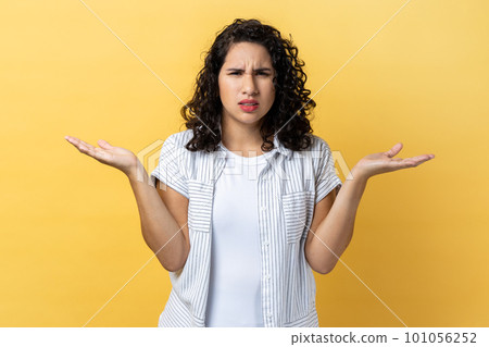 What do you want. Portrait of woman with dark wavy hair standing with raised hands and surprised indignant expression, asking what reason. Indoor studio shot isolated on yellow background. What do you want. Portrait of woman with dark wavy hair standing with raised hands and surprised indignant expression, asking what reason. Indoor studio shot isolated on yellow background. 101056252