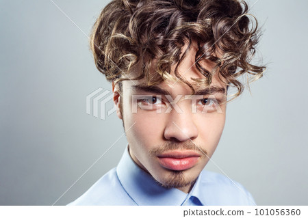 Portrait of handsome man with mustache and beard with curly hairstyle, wearing blue shirt, looking at camera with serious expression. Indoor studio shot isolated on gray background. Portrait of handsome man with mustache and beard with curly hairstyle, wearing blue shirt, looking at camera with serious expression. Indoor studio shot isolated on gray background. 101056360