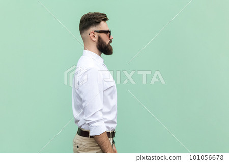 Side view portrait of handsome businessman wearing white shirt and black sunglasses standing with serious and confident facial expression. Indoor studio shot isolated on light green background. Side view portrait of handsome businessman wearing white shirt and black sunglasses standing with serious and confident facial expression. Indoor studio shot isolated on light green background. 101056678