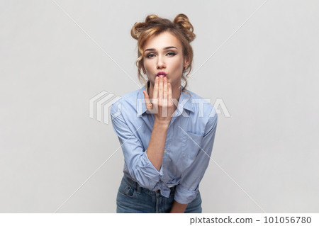 Portrait of romantic flirting blonde woman blowing kiss, demonstrates her good feelings, says goodbye on distance, wearing blue shirt. Indoor studio shot isolated on gray background. 101056780