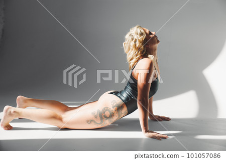 a sexy blonde with tattoos in a leather swimsuit performs sports exercises a sexy blonde with tattoos in a leather swimsuit performs sports exercises 101057086