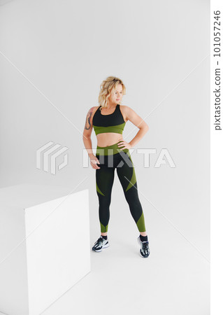 an attractive blonde in a black and green tracksuit poses on a white background. 101057246