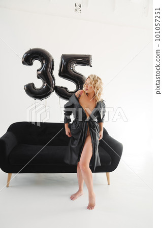 a naked blonde with tattoos in a black coat by a black sofa. birthday a naked blonde with tattoos in a black coat by a black sofa. birthday 101057251