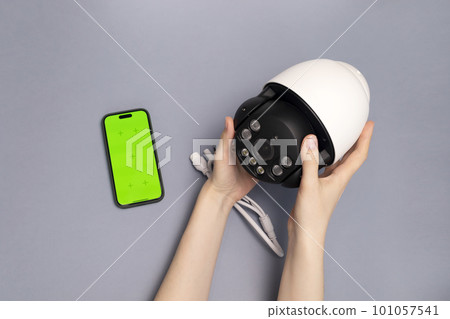 Human Hands Hold Surveillance IP Video Wireless Camera, Chroma Key Green Screen of Smartphone On Gray Background.Security Equipment For Smart Home, Online Remote App Monitoring, Control.Horizontal. 101057541