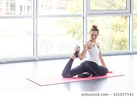 Portrait of athletic woman practicing yoga on mat and smiling, doing one legged king pigeon pose, warming up stretching muscles. Indoor shot with window on background. Portrait of athletic woman practicing yoga on mat and smiling, doing one legged king pigeon pose, warming up stretching muscles. Indoor shot with window on background. 101057542