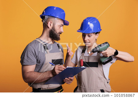 Engineers team looking at construction measurements on clipboard files, holding papers and power drill gun. Contractors talking about renovating project, preparing to work on refurbishment. 101058867