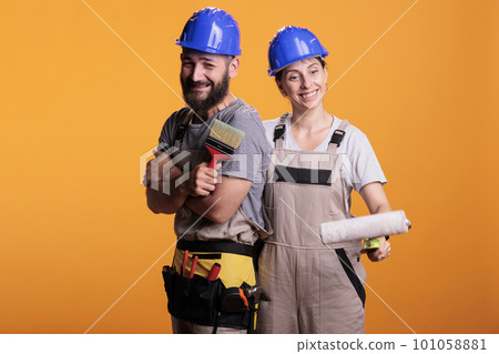 Team of contractors with paintbrush and roller in studio, working on painting job with tools. Construction workers experts wearing overalls and posing with brushes, doing renovation project work. Team of contractors with paintbrush and roller in studio, working on painting job with tools. Construction workers experts wearing overalls and posing with brushes, doing renovation project work. 101058881