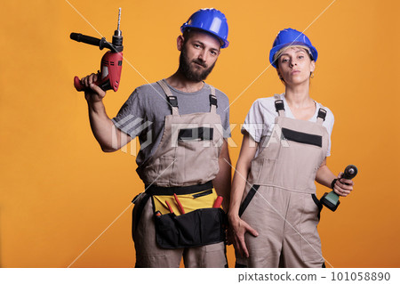 Man and woman renovators using drilling tools in studio, holding electric power drills for renovation work. Team of contractors working together on refurbishment project, using nail guns. 101058890
