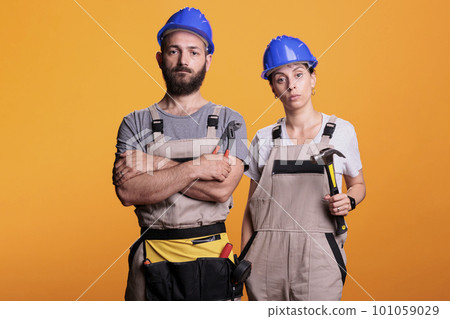 Team of building engineers holding renovating tools on camera, using sledgehammer and pair of pliers to work on renovation project. Builders posing with hammer and pliers over background. 101059029
