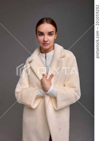 Beautiful fashionable woman in a cozy fur coat on a gray background positive girl posing at the camera in beautiful spring clothes 101059202