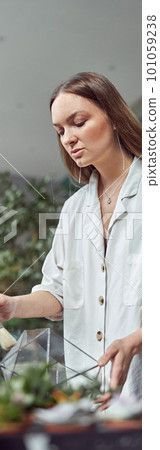 caucasian confident happy florist is working with composition made from glass stones and plants in botanic shop 101059238