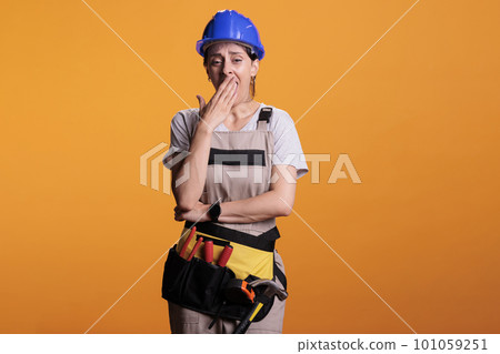 Sleepy overworked builder yawning and feeling tired, falling asleep wearing overalls in studio. Exhausted construction worker being fatigued and feeling burnout after building work. 101059251