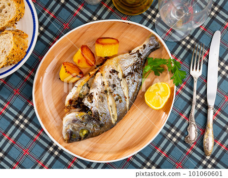 Baked in oven dorado fish with lemon and potatoes served on plate closeup 101060601