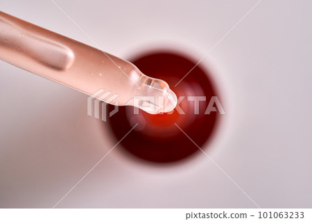 Pipette with pink cosmetic product on the background of a burgundy bottle. Pipette with pink cosmetic product on the background of a burgundy bottle. 101063233
