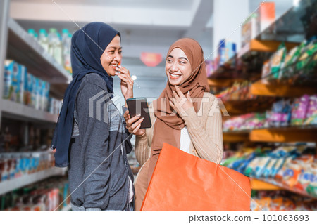 Two Muslim girls laughing while using a smartphone while shopping Two Muslim girls laughing while using a smartphone while shopping 101063693