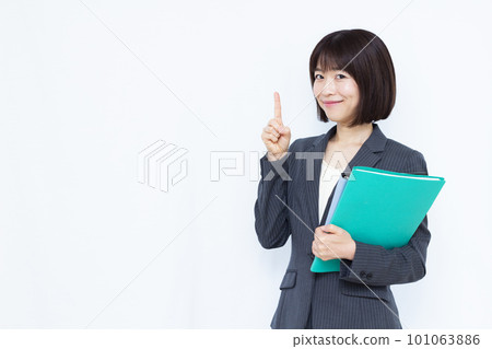 A business woman in her thirties in a suit who raises her index finger in front of a white background 101063886