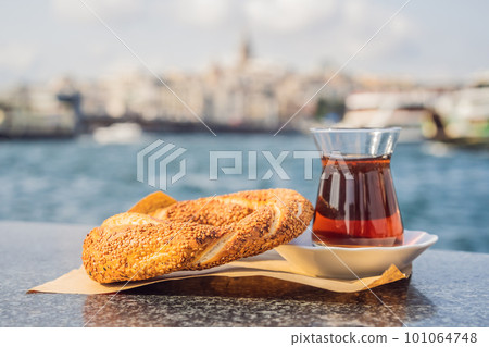 A glass of Turkish tea and bagel Simit against golden horn bay in Istanbul, Turkey. Turkiye 101064748